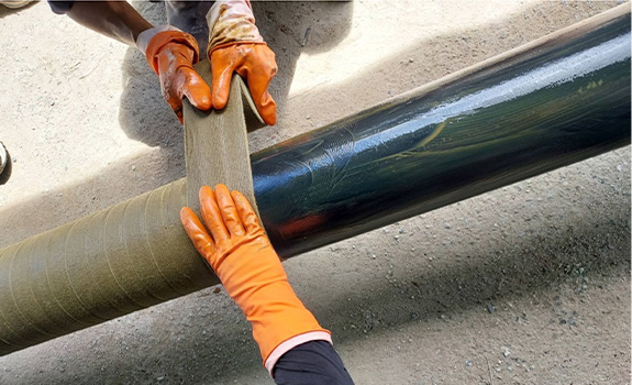 Workers in PPE gloves wrap a pipe with petrolatum tape