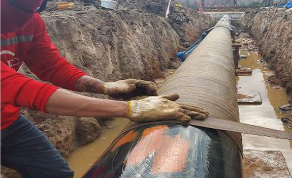 A man helps to wrap a petrolatum tape system around a pipe.