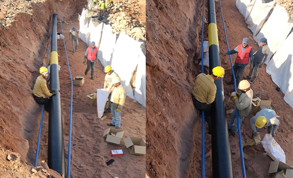 A contractor stands in a trench next to a pipe wrapped with protective PVC and bitumen tape.