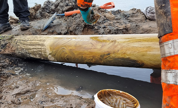 A gloved hand applied a brown paste from white tub to an exposed pipe