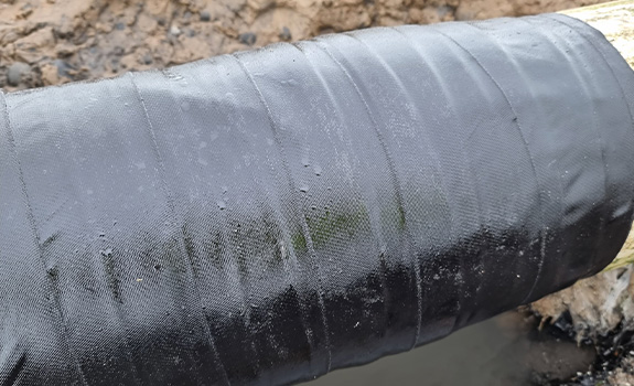 A close up of a pipe with a black tape wrapped around it, with beads of water on its surface