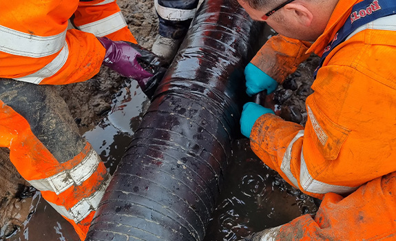 Workmen in high vis and protective clothing wrapping a wet tape around an exposed pipe