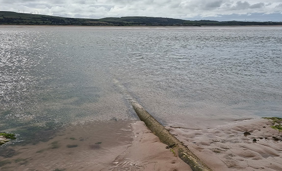 A half submerged pipe rising from a body of water with hills in the background
