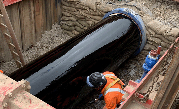 A pipe in a trench completely covered in a black liquid (Denso Primer D).