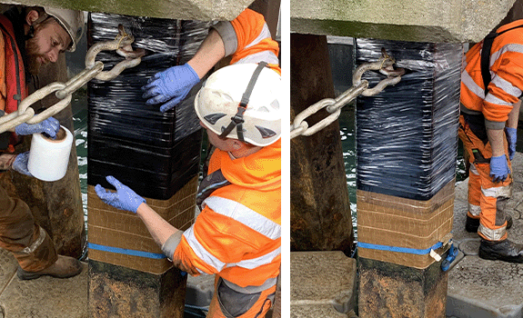 A clear cling-film being wrapped by two workers around the same pile, over the top of the black tape.