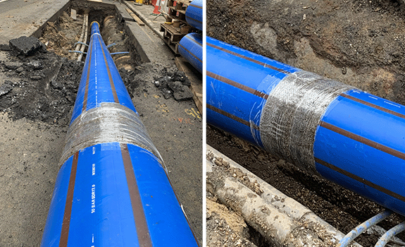 A pipe joint on a blue water pipe protected with Denso Bore-Wrap being pulled into a hole on a Central London Street.