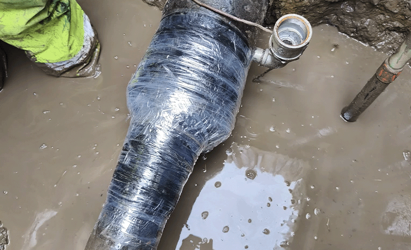 A casing end in a trench wrapped in a clear outerwrap, with muddy water in the background.